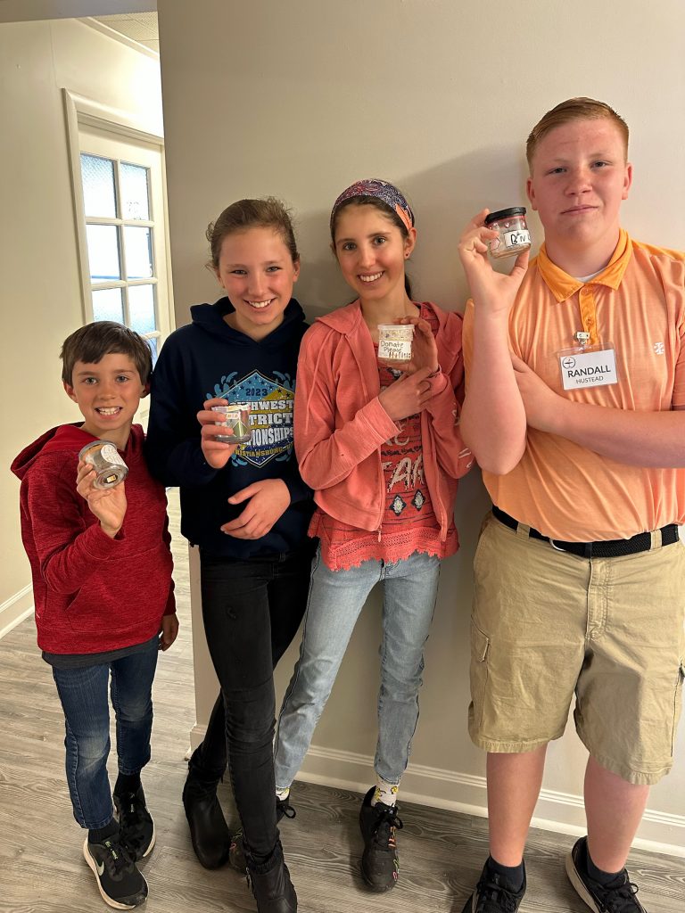 Four kids holding up jars