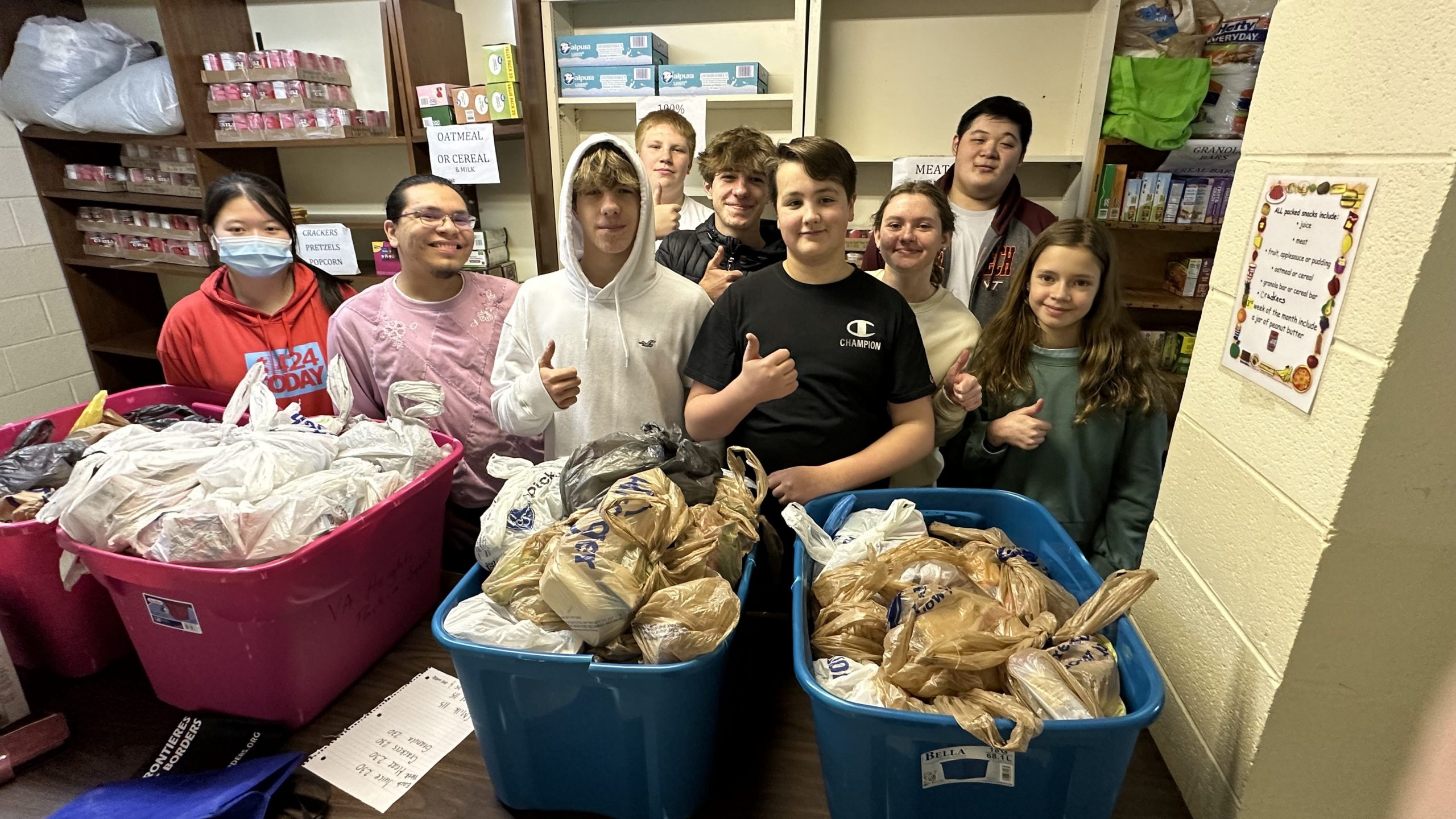 Teens giving a thumbs up with totes filled with bagged goodies
